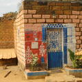 A small brick built house with a blue door and red wall painting