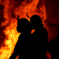 Figures in headdresses silhouetted against a large fire