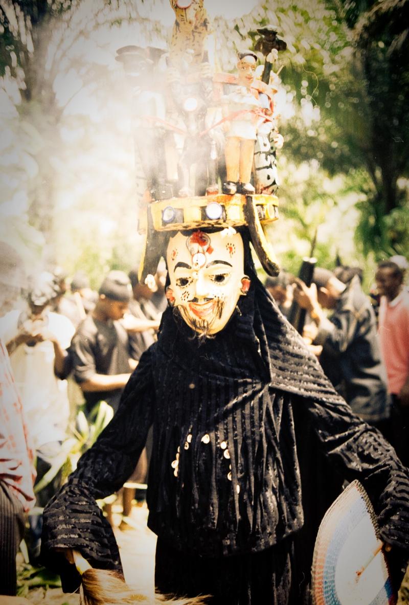 Large black figure parading in wooden mask with tall headress 