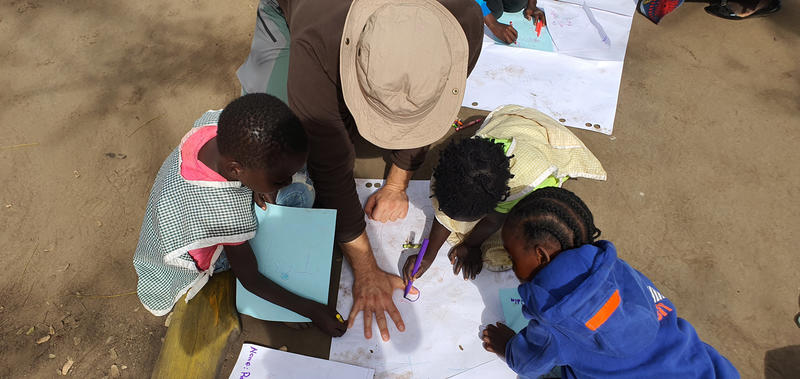 View of a group from above - children are drawing around a mans hand