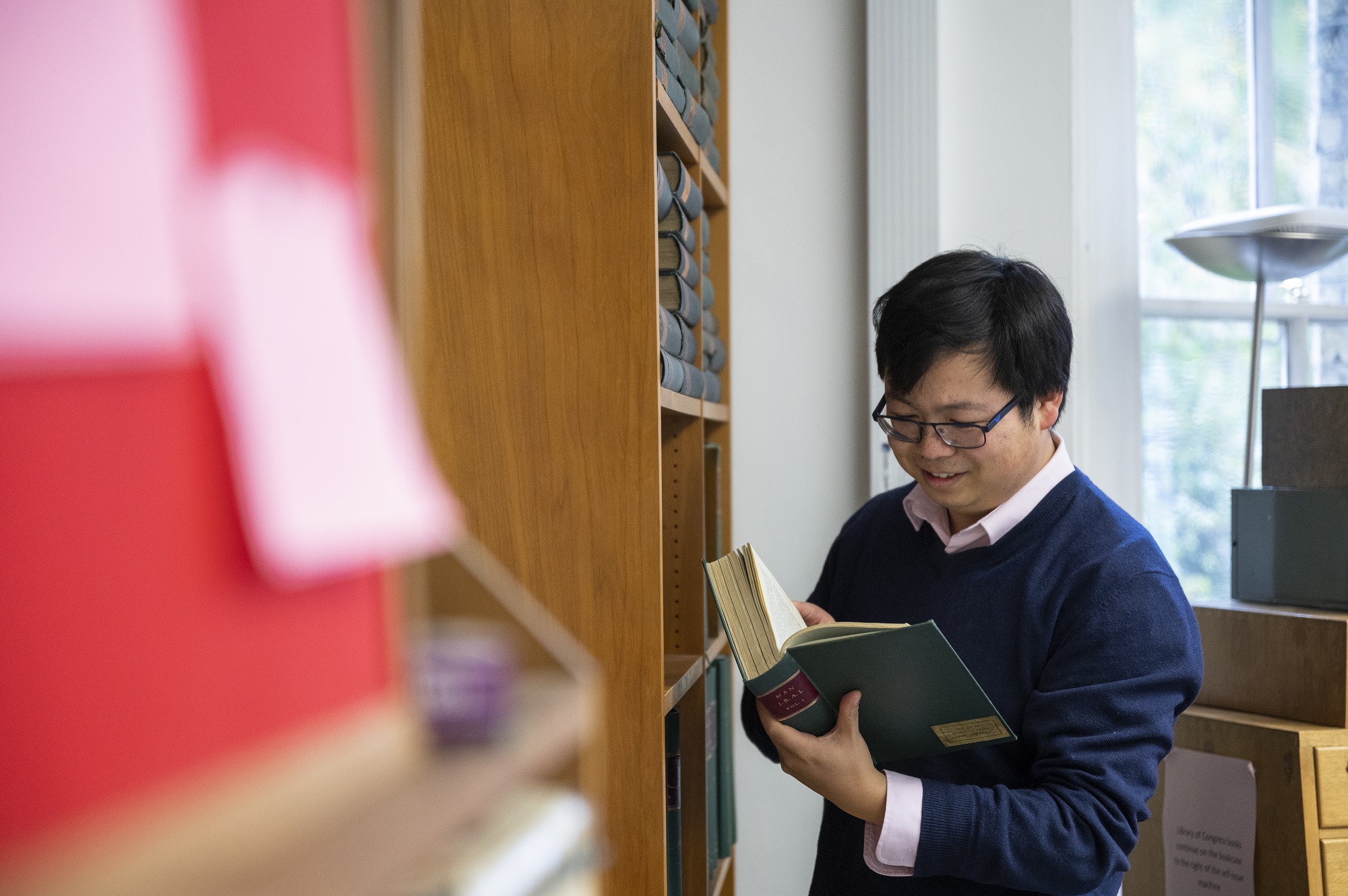 a male student reading standing whilst standing at book shelf