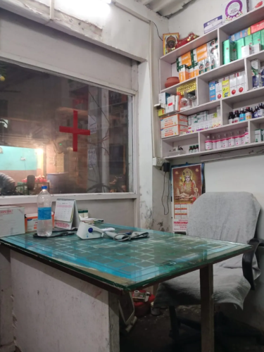 a makeshift office with a red cross on the window and medicines displayed behind the desk.