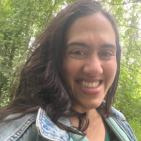 A woman smiling in a wood with a baby in a carrier