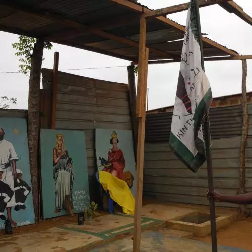 A small wooden shelter with three paintings of royalty underneath, man with flag in foreground