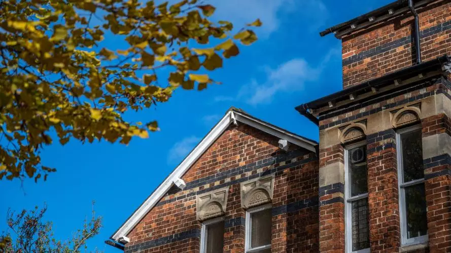 The top floor of a red-brick building, against a bright blue sky and next to a tree with autumnal leaves