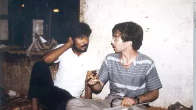 Two men seated cross legged on the floor in conversation