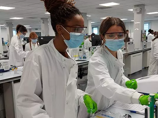 Two human sciences students at work in the lab wearing lab coats, face masks and gloves