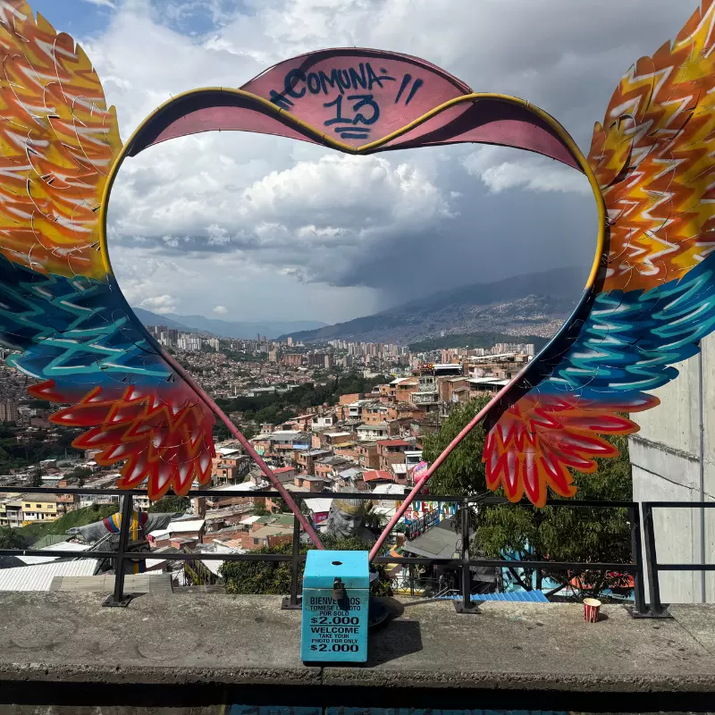 A view over a city in a mountainous landscape through a grafitti heart with honesty box